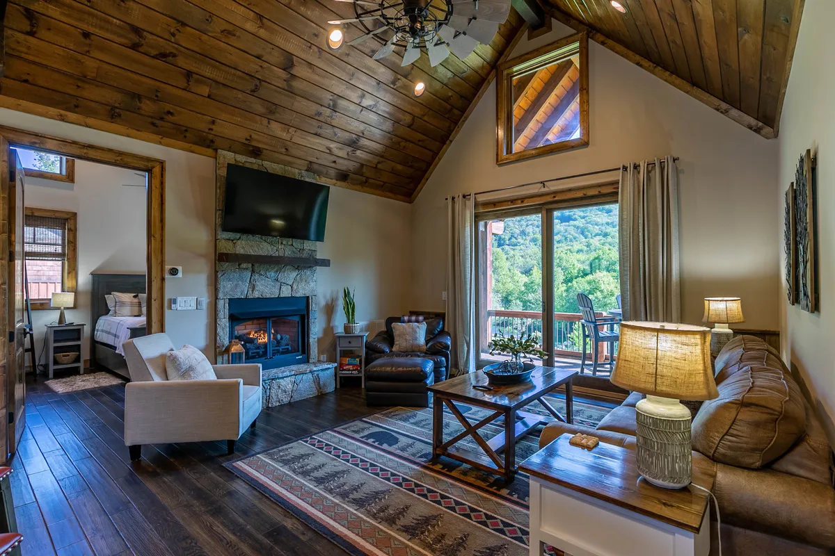 A cozy living area featuring a gas log fireplace, large windows providing expansive mountain views, comfortable seating arranged for conversation, and a central coffee table. Natural light fills the space, emphasizing its openness and warmth.