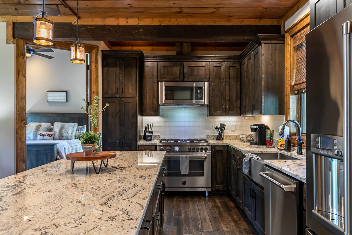 A kitchen featuring a granite countertop, rich wooden cabinetry, modern stainless steel appliances, and stylish pendant lighting. The setup is clearly designed for cooking and socializing, with an open, inviting layout.