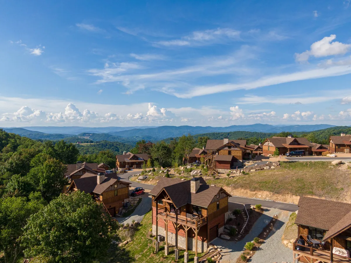 A cluster of charming wooden cabins nestled in a serene mountainous landscape, with rolling hills and a cloudy sky in the background. The setting exudes privacy and natural beauty, perfect for outdoor relaxation or sunset watching.