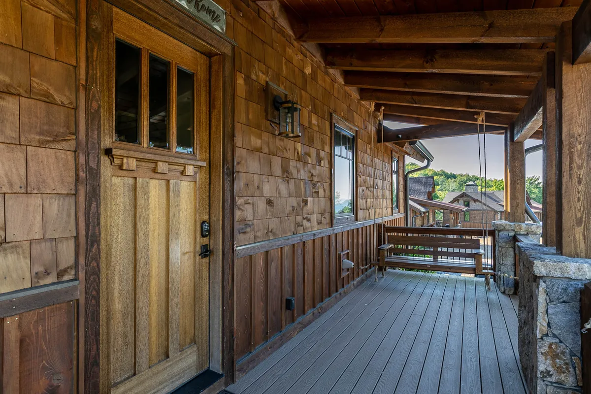 A cozy exterior shot focused on the wooden front door, shingle siding, stone accents, and a porch swing. The porch invites relaxation, while the front yard and visible surroundings suggest a welcoming, pet-friendly entry point to the home and community.