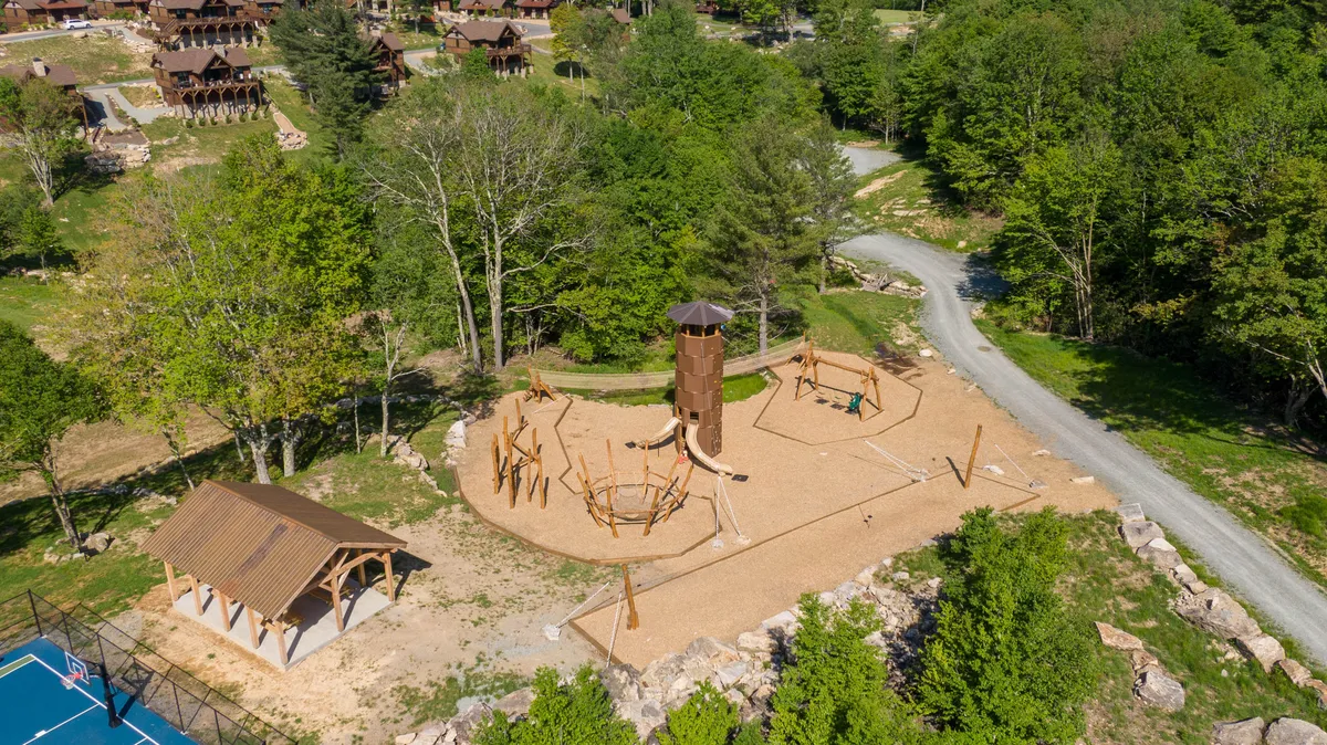 A lively exterior image, this scene features a playground, a basketball court, walking paths, and abundant trees, all suggesting spaces for both adult and family recreation. The area is clearly designed for activity, relaxation, and social interaction, framed by the beautiful natural surroundings.