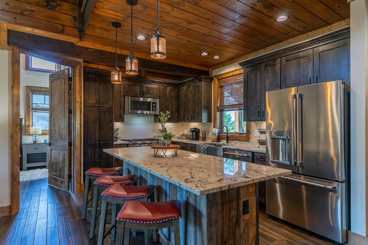 A view of the kitchen featuring granite countertops, warm wooden cabinets, bar stools for casual seating, and pendant lighting overhead. The layout suggests a communal, welcoming atmosphere ideal for family-style meals or quick snacks.