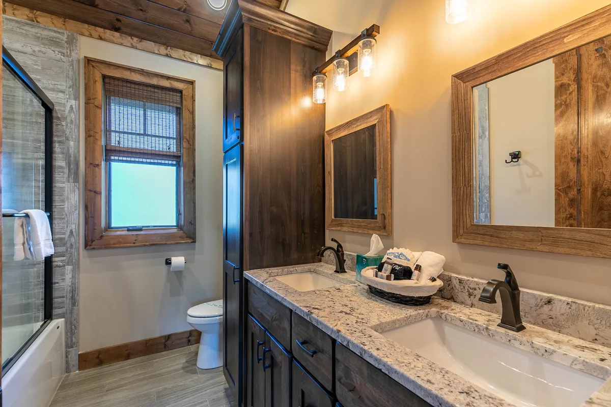 A functional and serene en-suite bathroom featuring a vanity with dual sinks, wooden cabinetry, large mirrors, and a glass shower enclosure. The design suggests comfort and ease for morning and evening routines.
