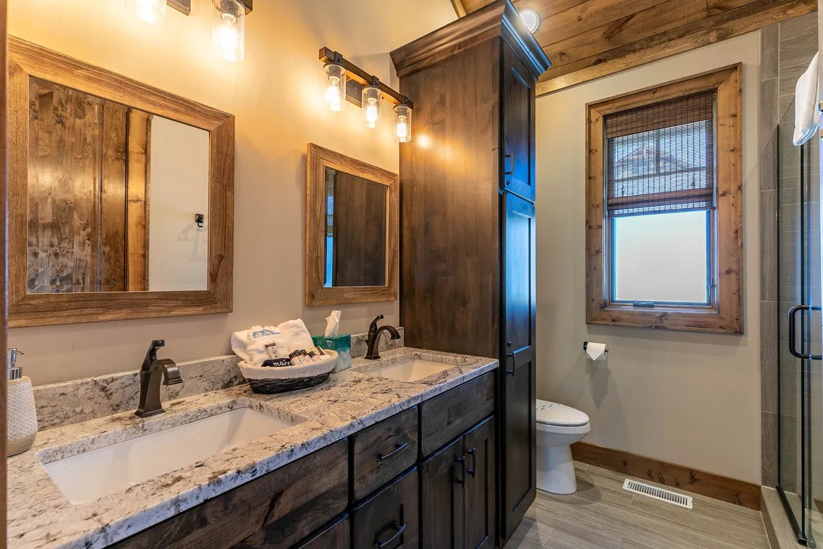 A bright en-suite bathroom with a double sink vanity, wooden cabinetry, large mirrors, and a visible shower area. The space feels serene and spa-like, ideal for unwinding or starting the day refreshed.